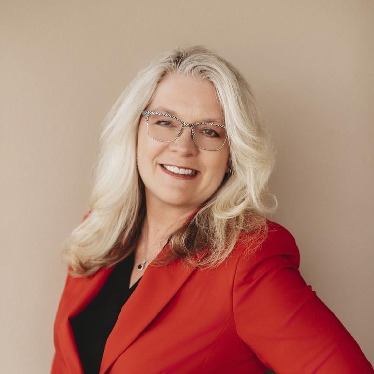 Smiling woman with blonde hair wearing glasses and a red jacket.